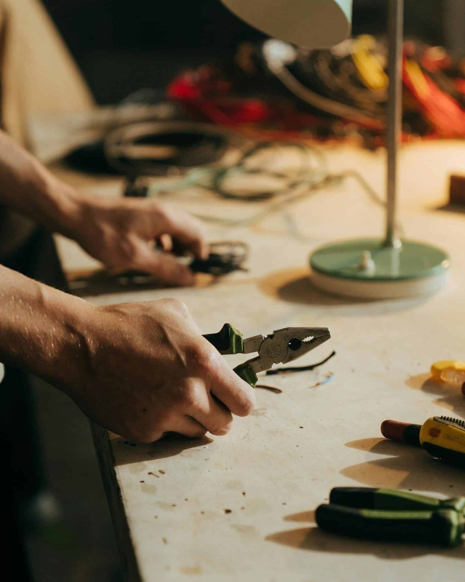 A craftsman using pliers on a workbench surrounded by tools in a dimly lit workshop.