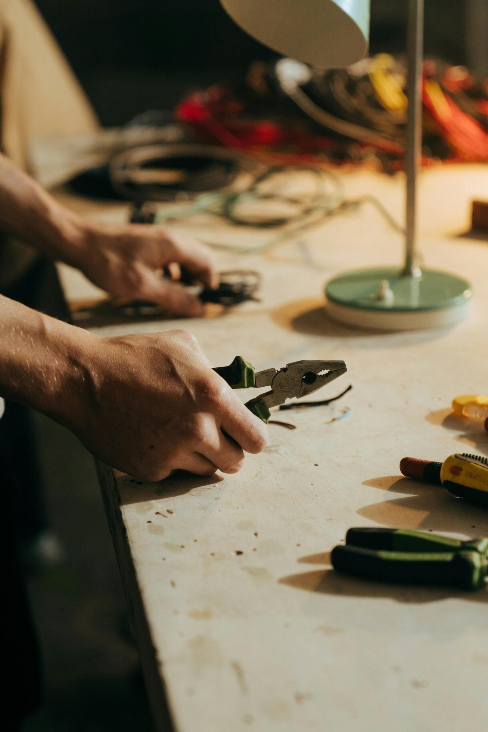 A craftsman using pliers on a workbench surrounded by tools in a dimly lit workshop.
