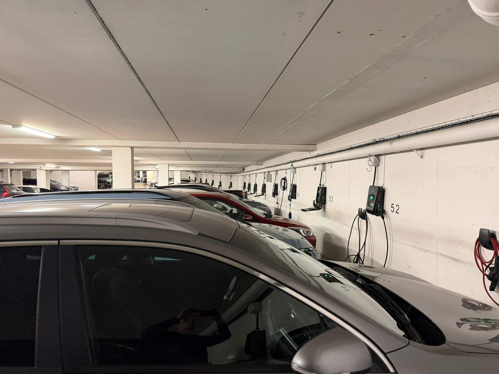 Rad av laddboxar vid numrerade platser i parkeringsgarage där flera elbilar laddar